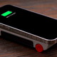 A smartphone charging atop the 8BitDo N30 Wireless Charger for Mobile sitting on a wooden desk.